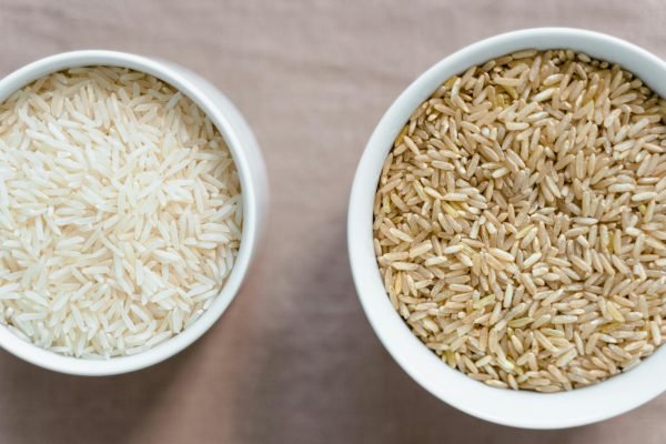 Top-down view of uncooked white and brown rice in bowls, showcasing healthy dietary choices.